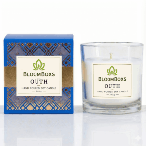 A lit oudh scented candle in an amber glass jar, casting a warm glow.